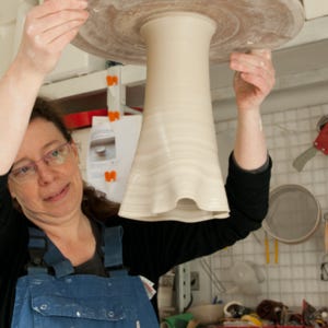Jeannine Vrins is shaking a wheel thrown vase upside down to make its rim wavy